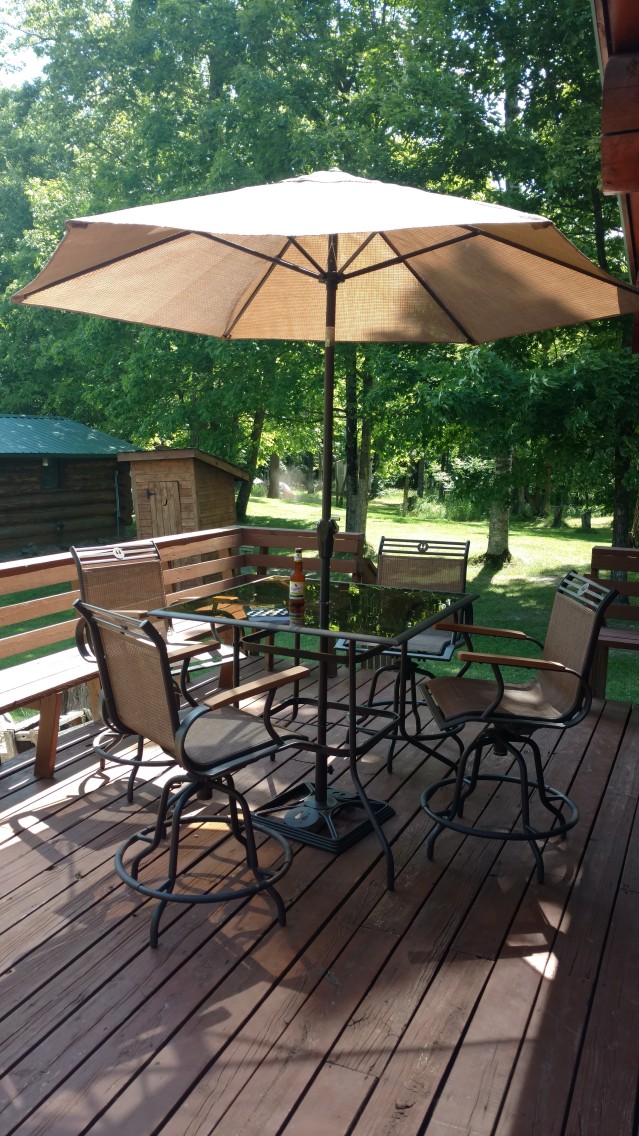 author's deck, with patio furniture, umbrella, and a book and a beer.