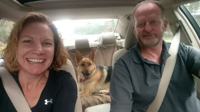 Selfie of the author and her husband in the car, with their German Shepherd in the backseat.