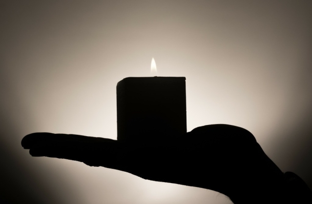 Silhouette of a flat palm holding a lit column candle.