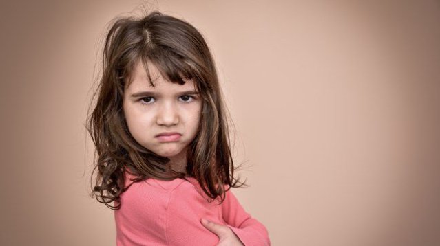 Young girl standing sideways crossing arms and looking directly at you with an annoyed, frustrated look