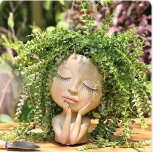 a planter of a woman's head resting her chin on her hands, the plant is her hair