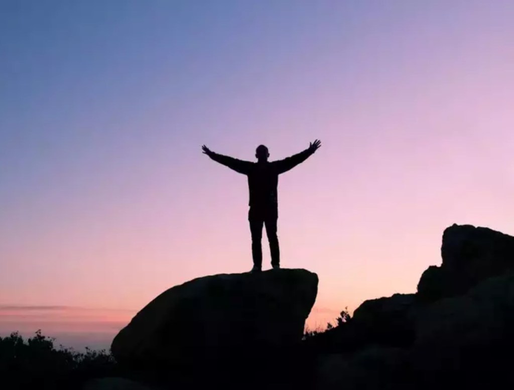 shilhouette of a man facing sunrise with arms outstretched