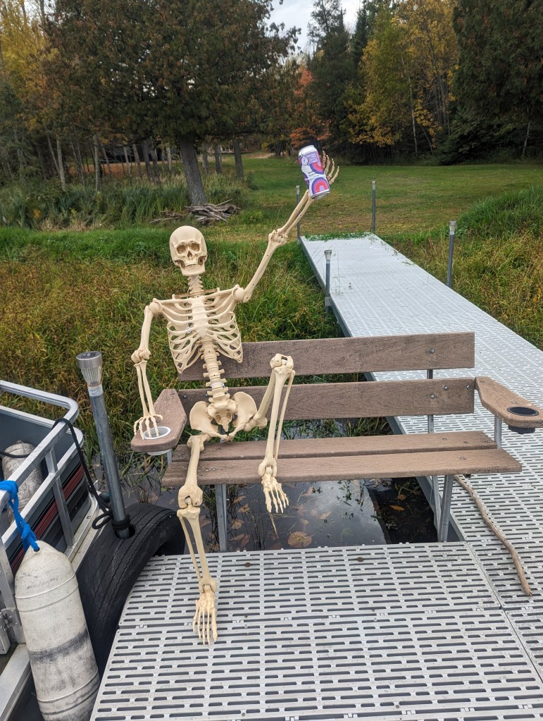 a beautiful fall day with a poseable five foot skeleton sitting on a bench and the end of the dock, one knee up and one arm raising a beer on 