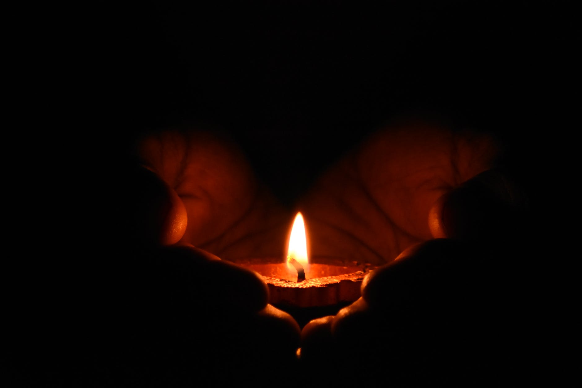 two hands holding one candle in the dark
